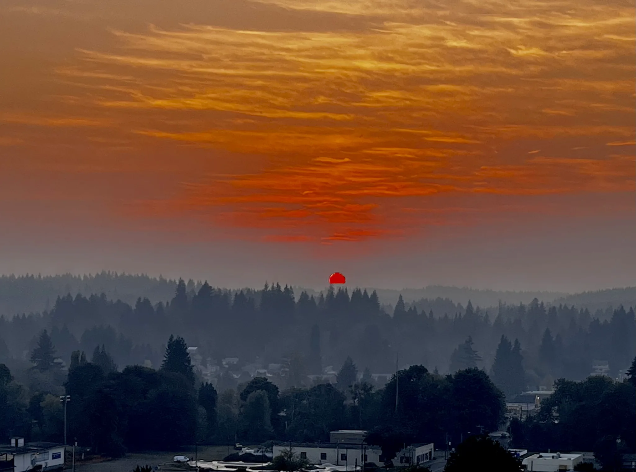 The sun a red disc through wildfire smoke, setting over the hillside property