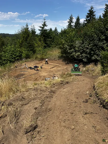 Site cleared and the building footprint staked out, sod cutter opening the new access path.